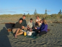 Mauricio, me (Nicholas), Haydn, Paul, Snaiet, and Denise pose for a photo while eating fish 'n' chips. In the background, a couple and their dog appear on the sand dunes.